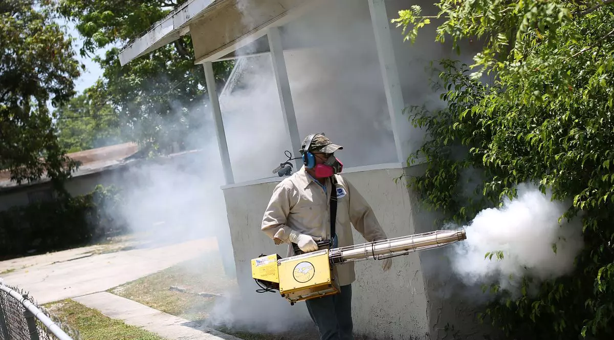 Un bărbat dă cu insecticid împotriva țânțarilor într-o zonă verde de lângă o casă, iulie 2026