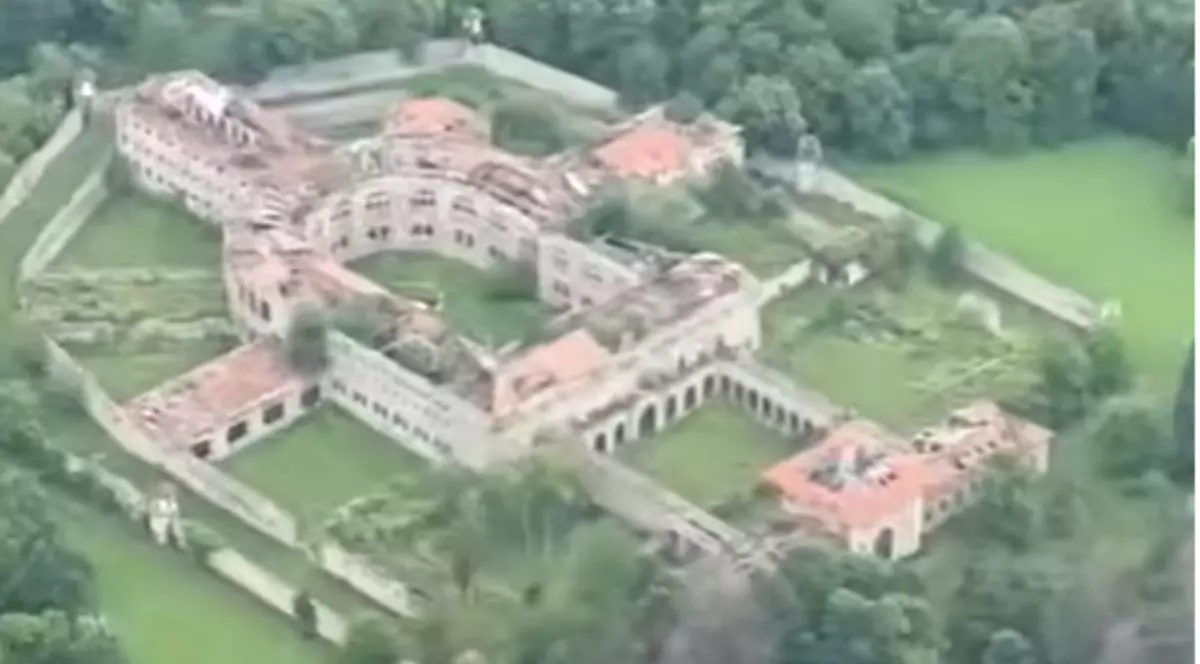 Imaginea surprinde o vedere aeriană a unui complex arhitectural de mari dimensiuni, înconjurat de ziduri și spații verzi, cu o curte interioară de formă circulară. Clădirea are acoperișuri din țiglă și este amplasată într-o zonă împădurită, ceea ce evidențiază amploarea și poziționarea izolată a ansamblului.