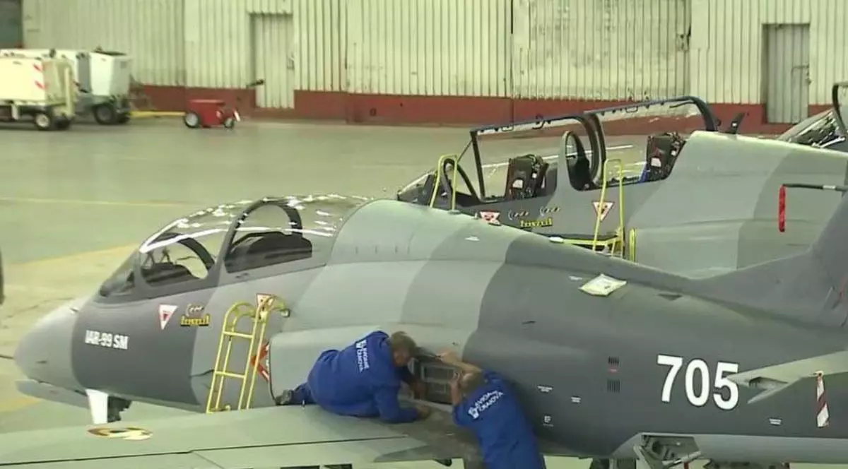 Doi ingineri de la Avioane Craiova, îmbrăcați în combinezoane albastre, lucrează la un avion IAR-99 SM de culoare gri, într-un hangar