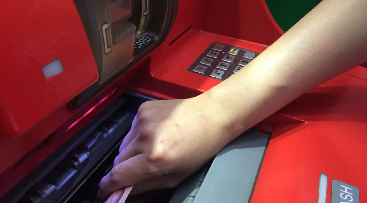 Cine poate retrage banii din contul unei persoane decedate - Imagine cu o mână de femeie care extrage bani dintr-un bancomat roşu.