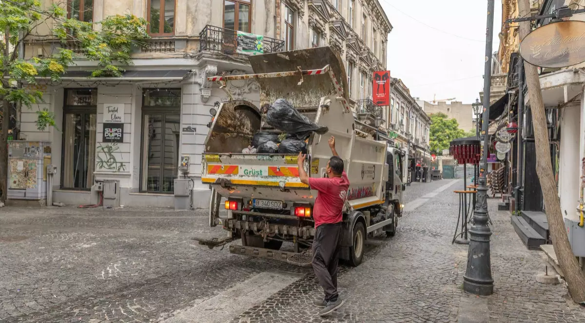 O mașină de gunoi în centrul Bucureștiului, un bărbat adună sacii cu deșeuri și îi aruncă în camion