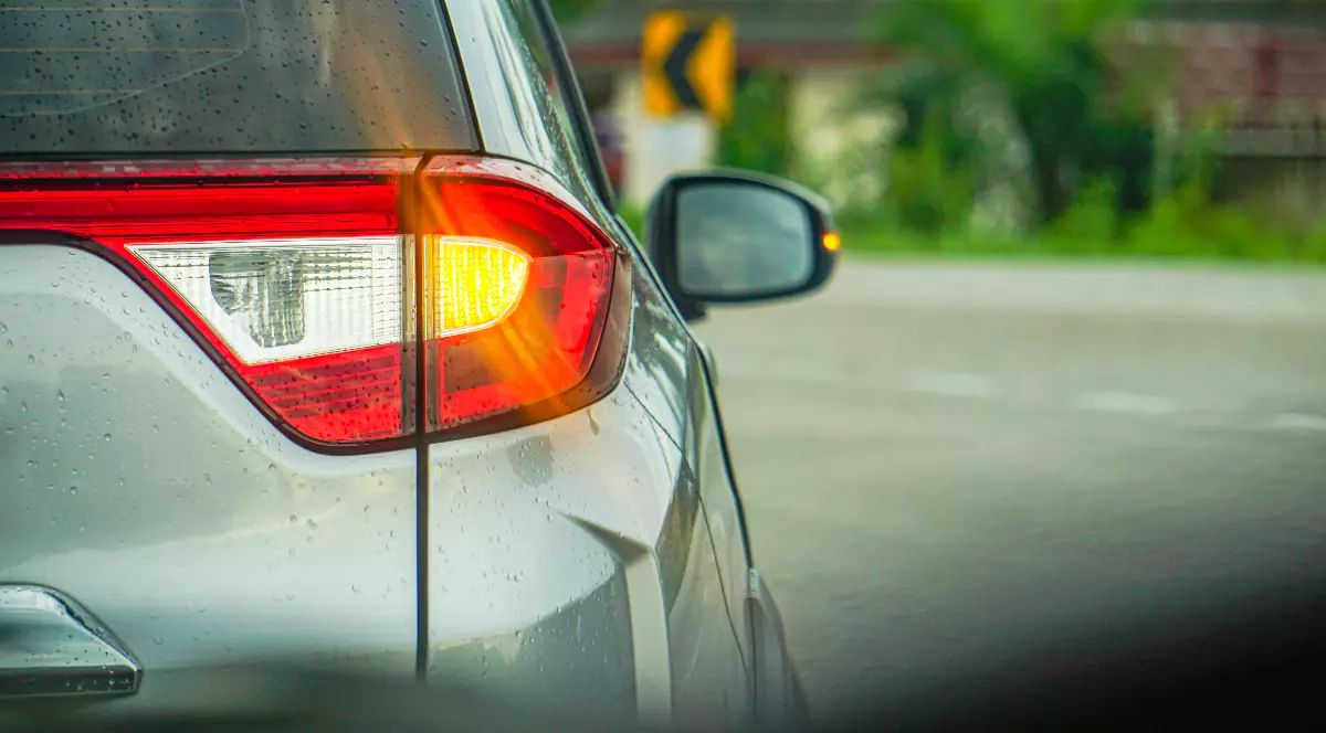 Un șofer care conduce o mașină gri și semnalizează dreaptă, la farul din spate al autoturismului se vede lumina galbenă