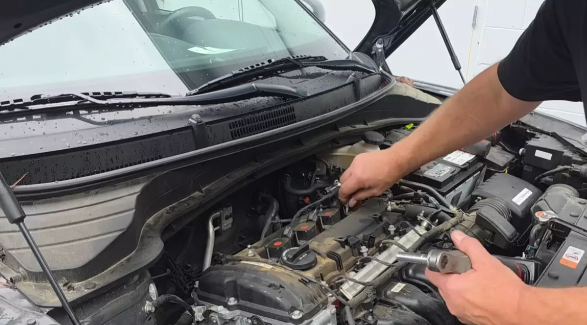 Un bărbat cu tricou negru care lucrează la compartimentul motor al unei mașini