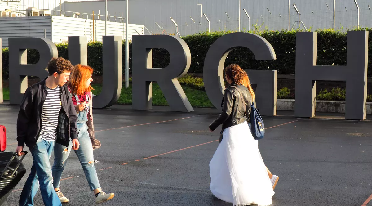 O mireasă roșcată cu o rochie albă, peste care are o geacă de piele, în aeroport, în timp ce pleacă în vacanță