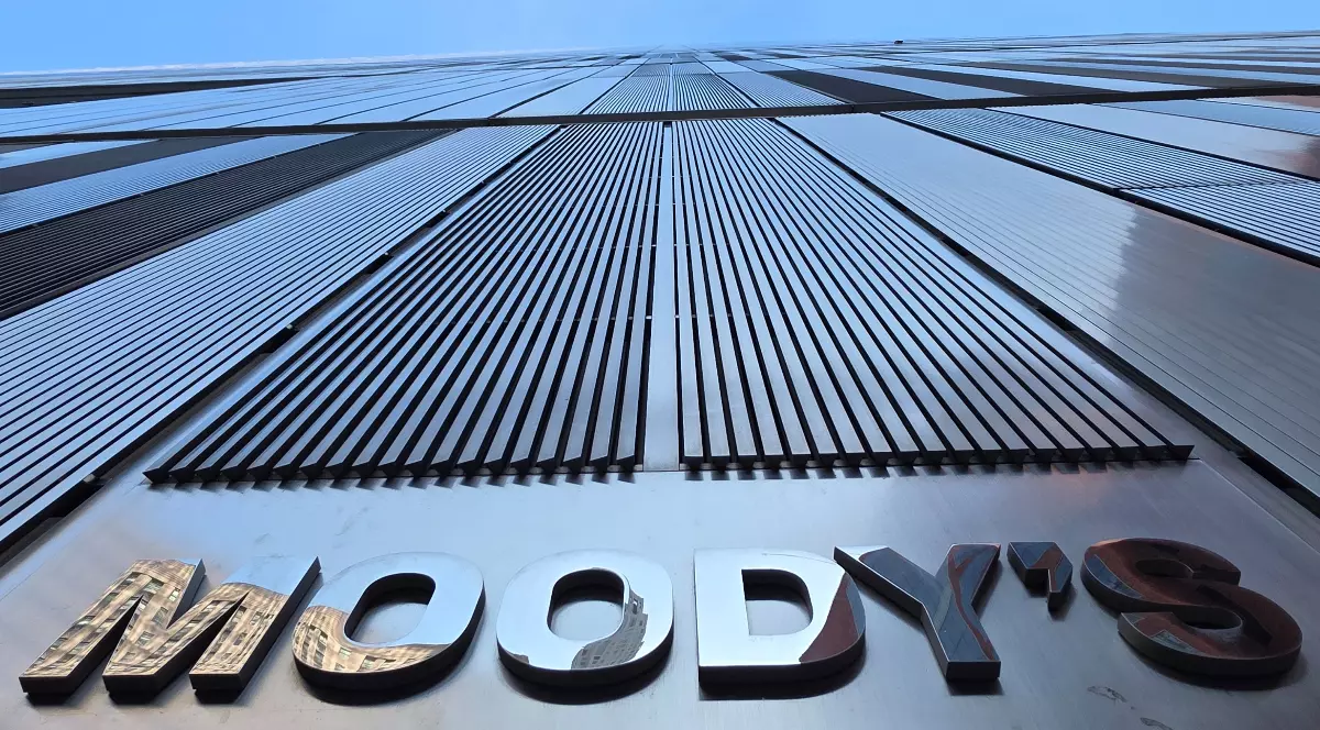 Imaginea prezintă o vedere alb-negru în perspectivă de jos în sus a fațadei unei clădiri moderne, pe care este inscripționat numele agenției Moody's.