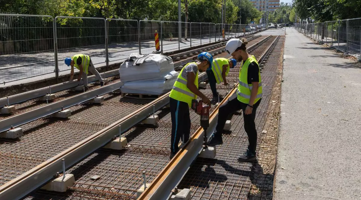 Muncitori îmbrăcați cu echipamente de protecție și căști pe cap, care lucrează la șinele de tramvai pe bulevardul 1 Decembrie 1918 din București, în august 2026