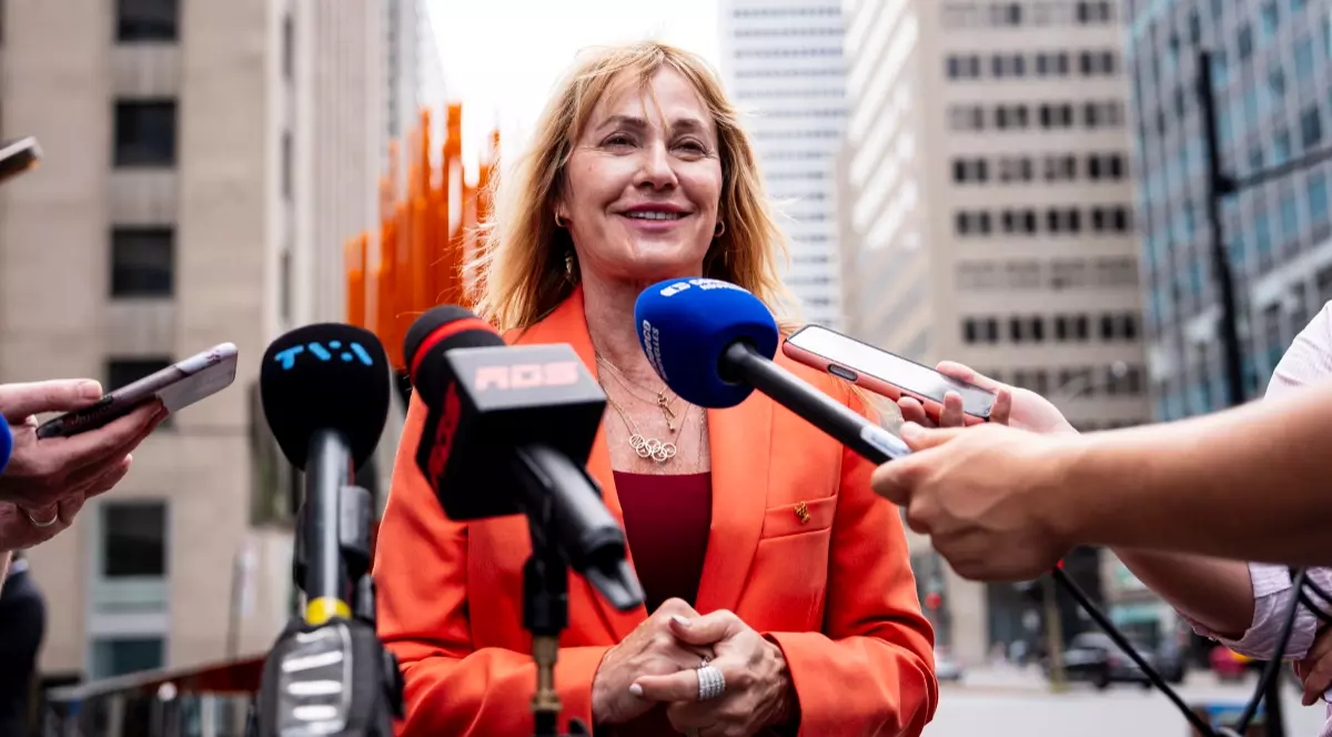 Nadia Comăneci, îmbrăcată într-un costum portocaliu, în timp ce ține o conferință de presă în Montreal la aniversarea a 50 de ani de la primul 10 din istoria Jocurilor Olimpice