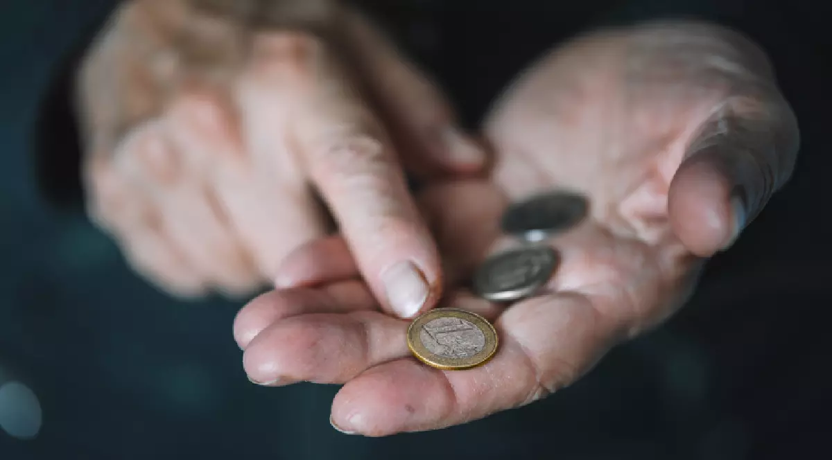 Un pensionar ține într-o mână trei monede euro, în timp ce le arată cu cealaltă mână