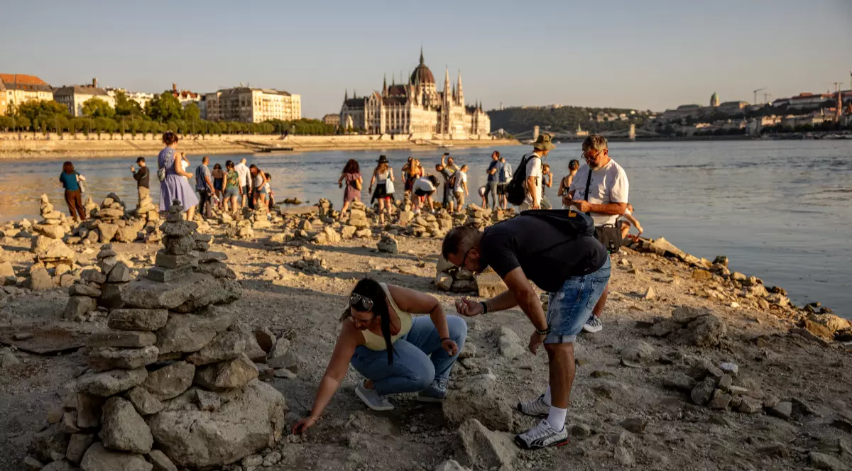 Turiștii și localnici din Budapesta, în timp ce se plimbă pe maul Dunării și adună pietre