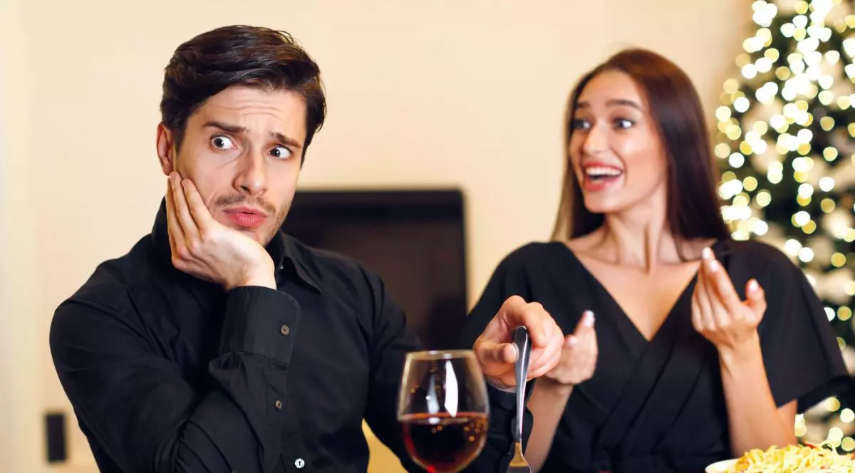 Un cuplu tânăr la o întâlnire într-un restaurant; bărbatul are o expresie amuzantă de dezamăgire și șoc, se simte stânjenit în timp ce ascultă o femeie entuziasmată vorbind.