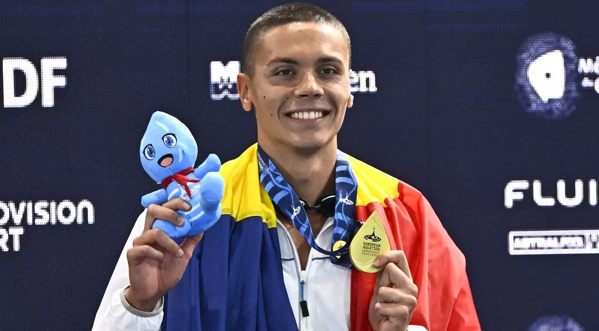 David Popovici ține steagul tricolor pe podiumul de premiere, după ce a cucerit aurul în proba de 100 metri la Campionatul european de laParis, 12 august 2026