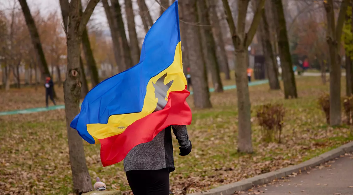 Un barbat alearga in parc infasurat intr-un steag tricolor