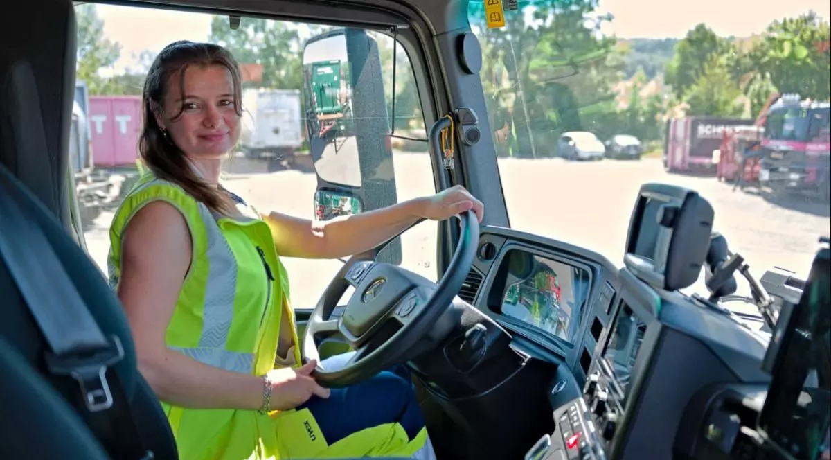 O româncă, îmbrăcată cu o vestă verde fosforescent, este la volannul unui camion de gunoi, în Germania