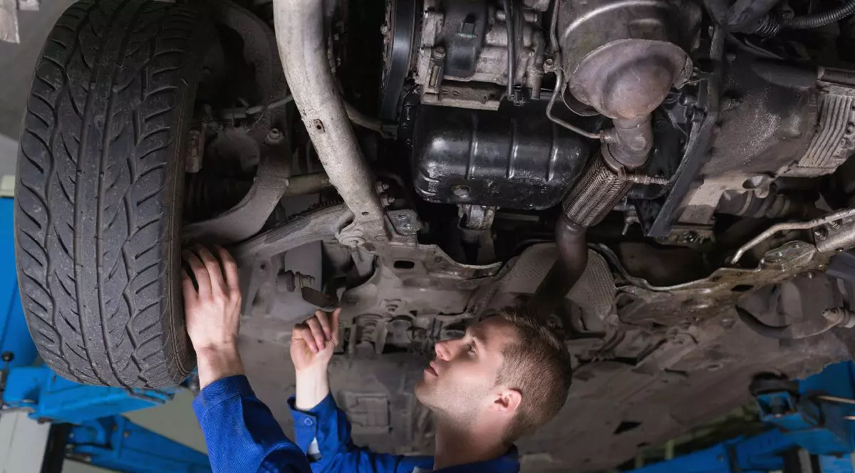 Un mecanic în salopetă albastră repară o mașină, stând sub ea