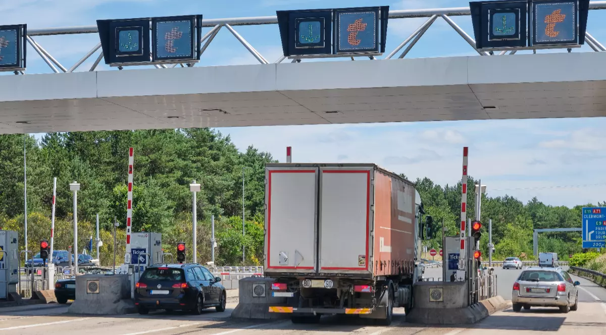 Imaginea înfățișează un camion și câteva autoturisme trecând prin porțile unei stații de taxare de pe o autostradă din Franța.