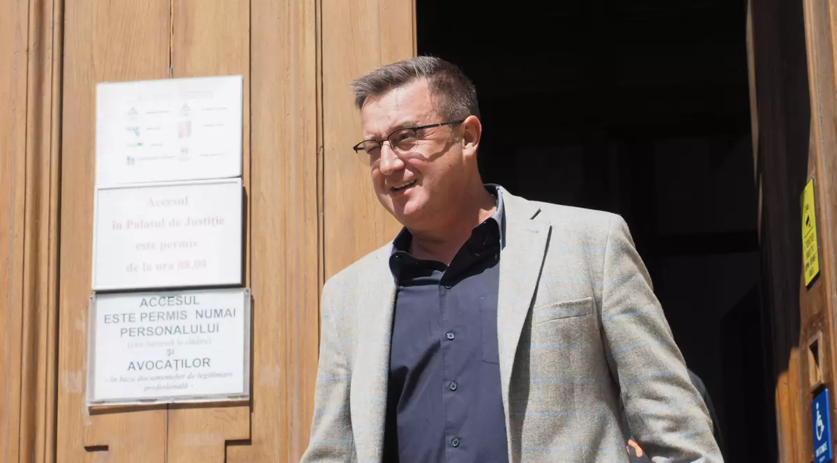 Un barbat in sacou bej si camasa gri iese pe usa unui tribunal