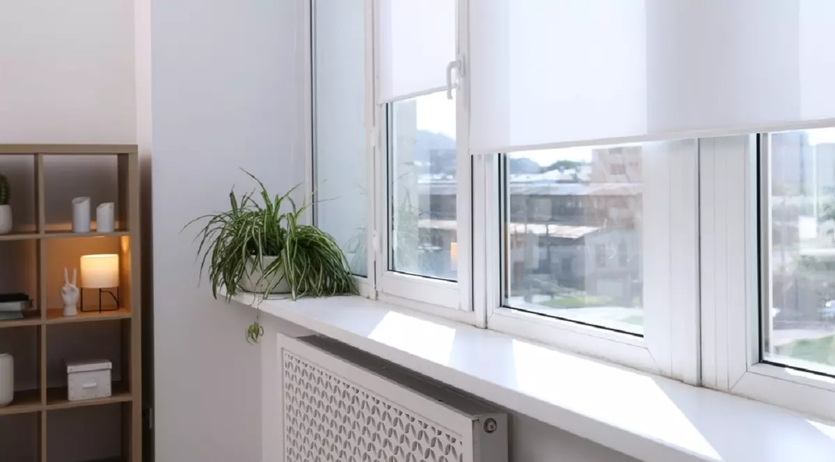 Cum blochezi căldura de la geamuri vara - Imagine cu storuri albe la ferestrele unei sufragerii dintr-un bloc