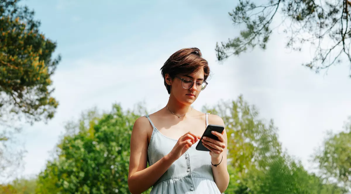 O femeie care ține un telefon în mână, poartă o rochie albastră și tastează un mesaj