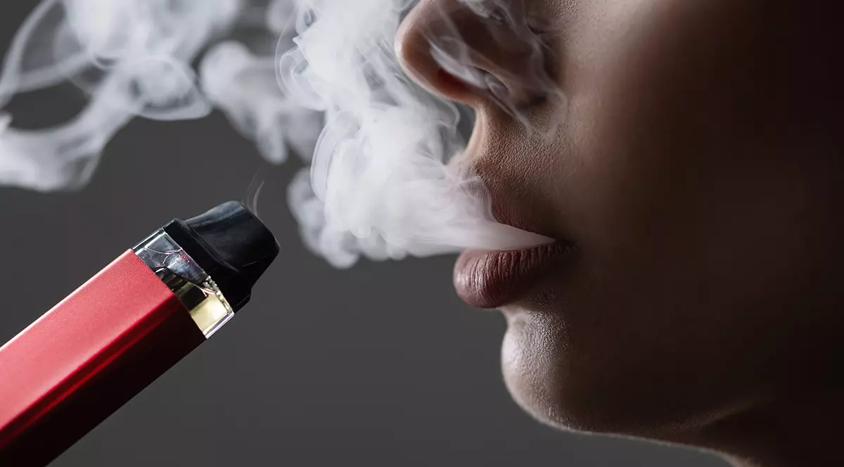 Un plan apropiat cu gura unei persoane care expira și inhalează aburi dintr-o tigare electronică grena.