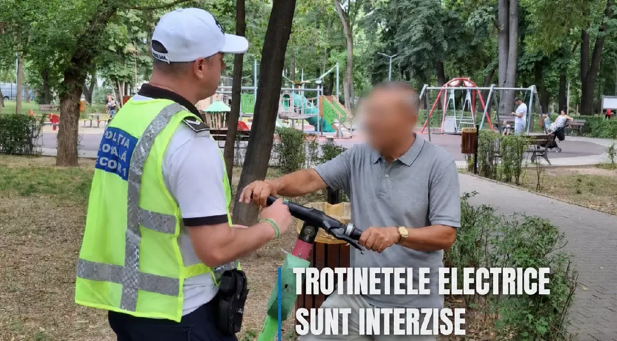 Un politist local il amendeaza pe un bărbat care circula pe o trotineta electriva verde intr-un parc