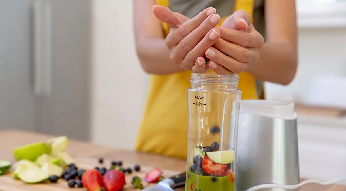 O femeie care face un smoothie la un blender în care pune multe fructe.