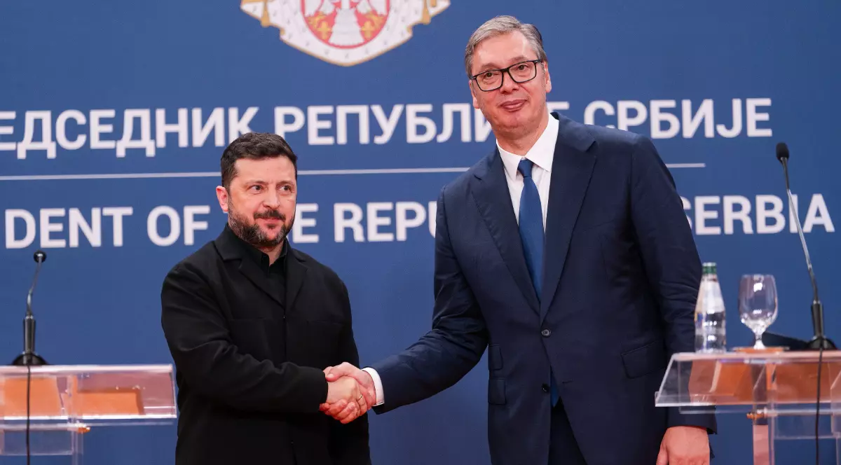În imagine, Volodimir Zelenski și Aleksandar Vučić apar împreună la o conferință de presă, în fața steagului și a însemnelor prezidențiale ale Serbiei. Cei doi lideri își strâng mâna, zâmbind, în timpul întâlnirii oficiale de la Belgrad.