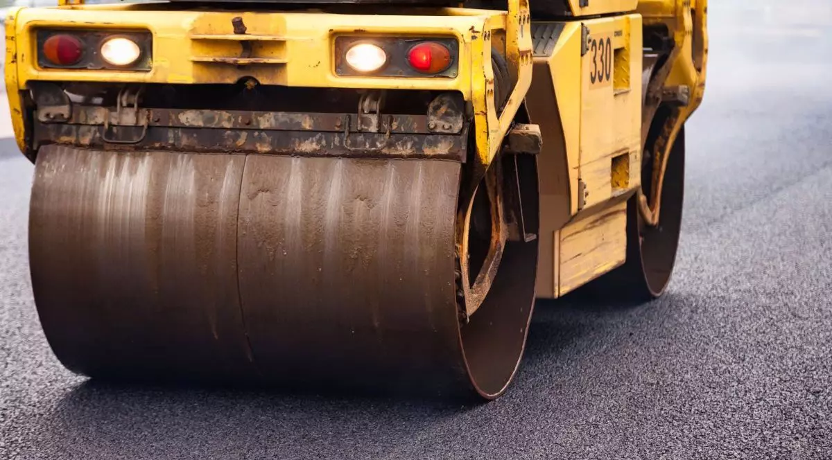 Muncitorii pun beton asfaltic pe un drum urban folosind echipamente de pavare.