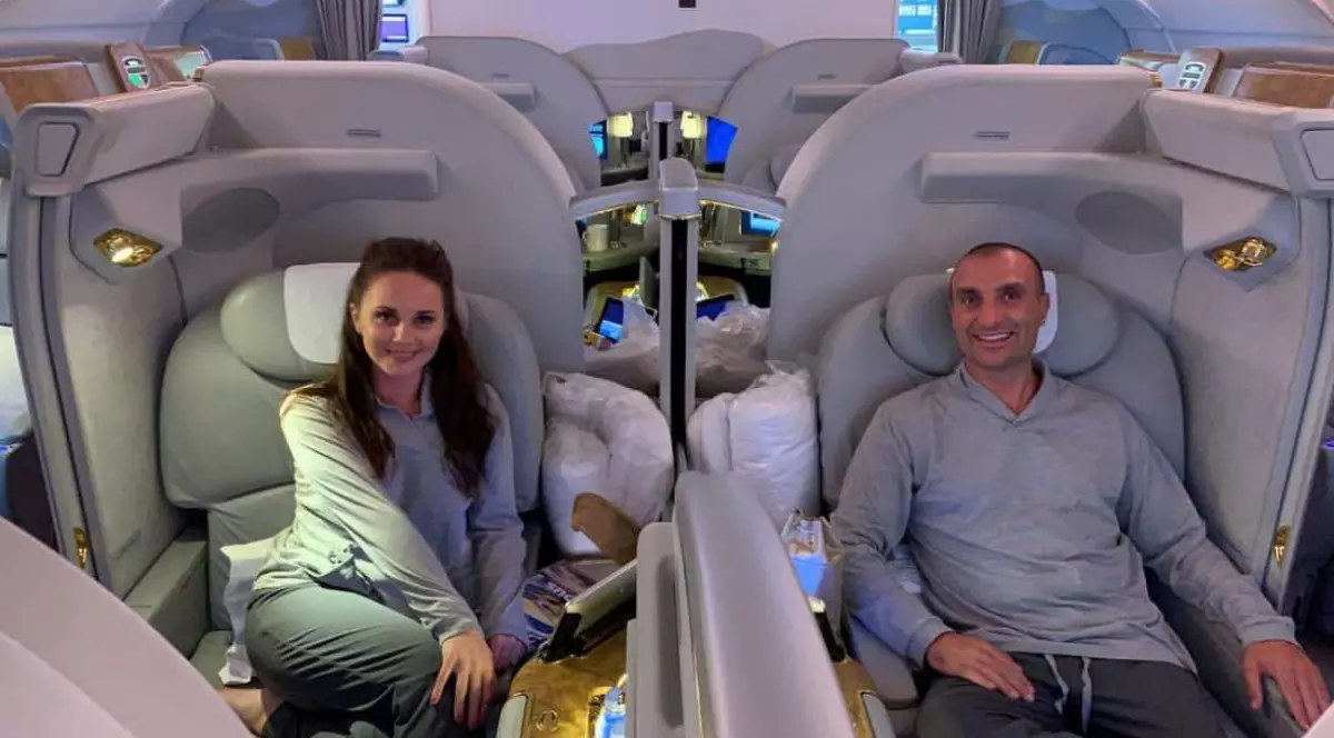 Un bărbat și o femeie la bordul unui avion, stau în fotoliile de la Clasa I și zâmbesc în fața camerei