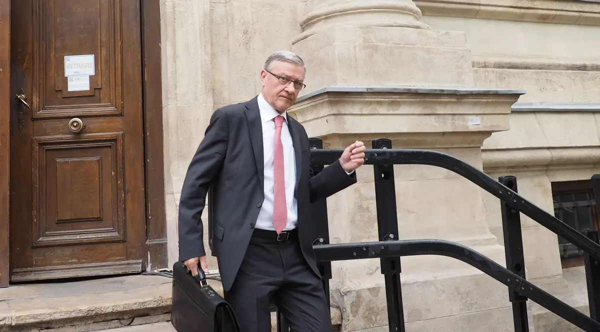 Un barbat in costum negru si camasa alba cu cravata roz iese din tribunal