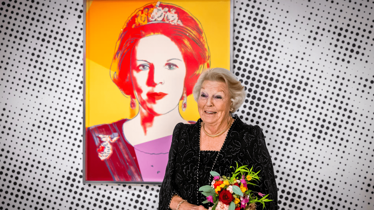 o femei cu un buchet de flori în mână, iar în spate, pe perete, o serigrafie a reginei Beatrix