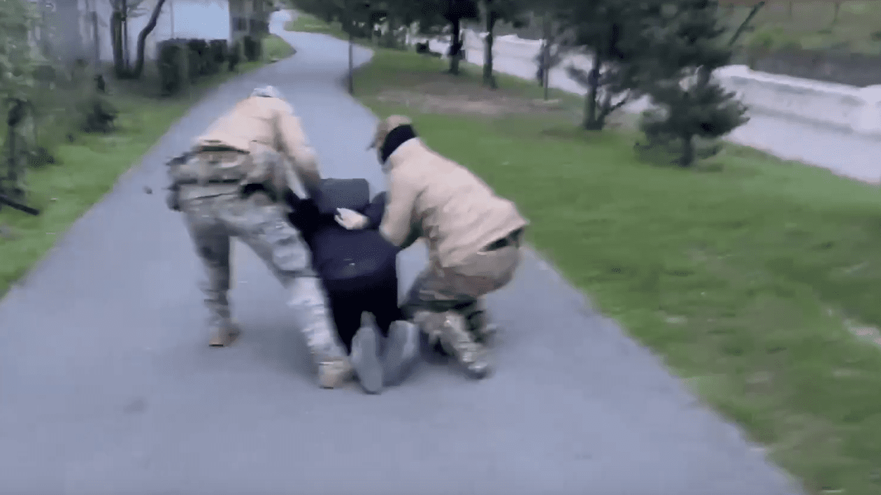 un bârbat, pus în genunchi pe asfalt de doi agenți ruși
