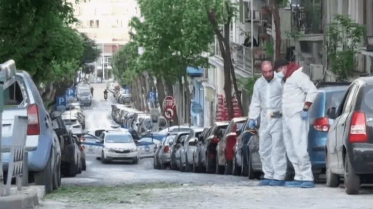 doii polițiști în combinezoane albe, pe o stradă cu mașini parcate de o parte și de alta, fac cercetarea la locul exploziei