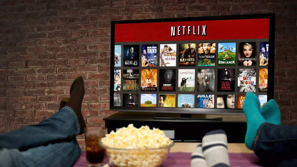 Netflix este aplicația cu cele mai mari venituri în 2017. Care sunt cele mai profitabile aplicații și jocuri de mobil. Televizor cu Netflix deschis și oameni vizionând cu popcorn lângă