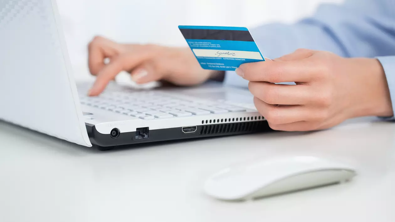 Tentativă de înșelătorie în numele Altex și eMAG, după cea cu Lidl. Două mâini de bărbat, deasupra unei tastaturi. În cea stângă ține un card bancar, iar cu cealaltă tastează