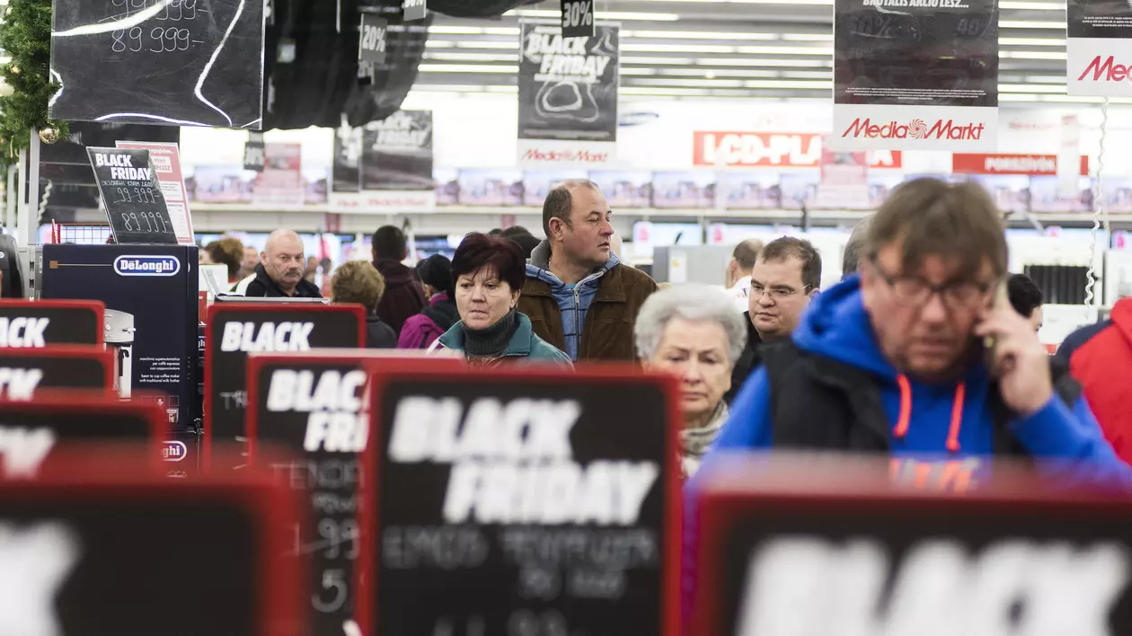 Altex, Media Galaxy și evoMag dau startul reducerilor de Black Friday începând cu 1 noiembrie. Oameni la coadă cu semne de reduceri de Black Friday pe lângă ei