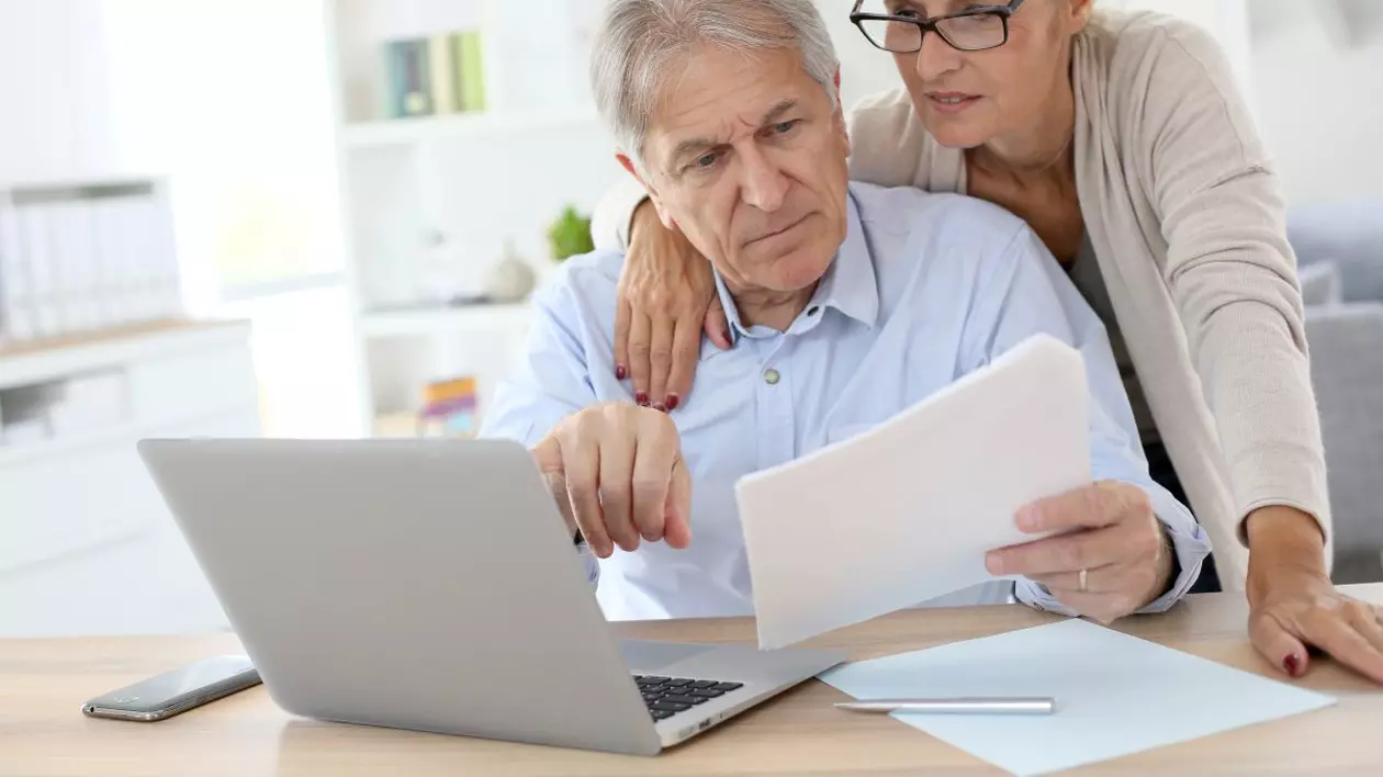 Românii nu ar trebui să renunțe la Pilonul II de pensii, consideră specialiștii. Cuplu de pensionari care calculează taxele în fața unui calculator