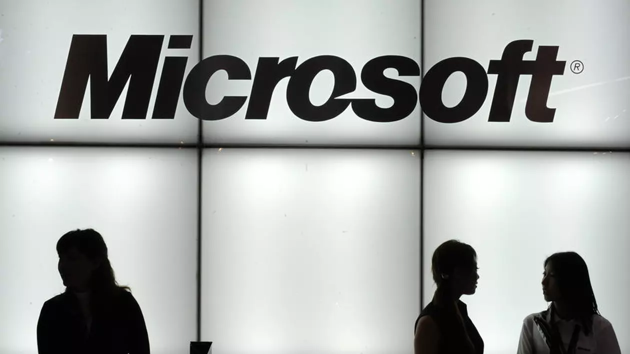 După Apple, a venit rândul Microsoft să avertizeze asupra efectelor epidemiei de coronavirus: gigantul american a anunțat că vânzările pentru sistemul de operare Windows și divizia sa de PC-uri nu se vor ridica la nivelul anterior. Logo Microsoft luminat, cu trei siluete de oameni în față