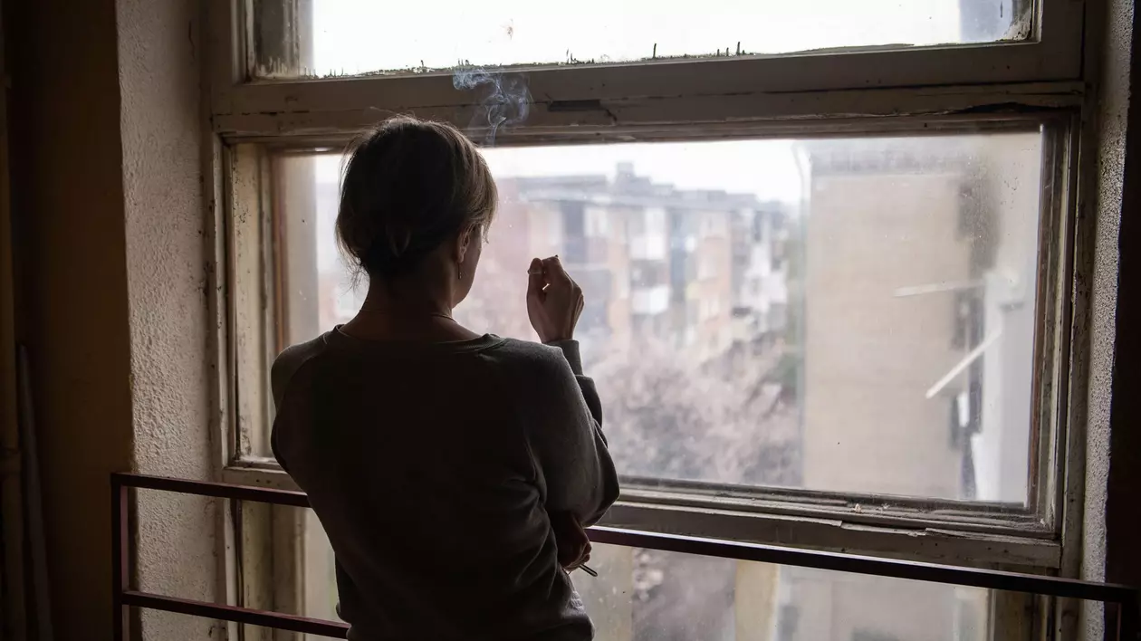 O femeie privește pe fereastră într-un bloc din Harkov, oraș bombardat de ruși încă din prima zi de război, 24 februarie. Foto: Profimedia