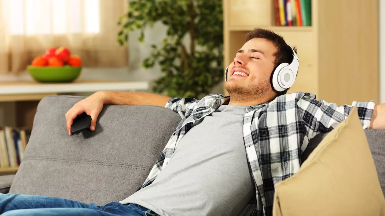 Curatare casti mobile- Un tanar sta relaxat pe canapea si asculta muzica