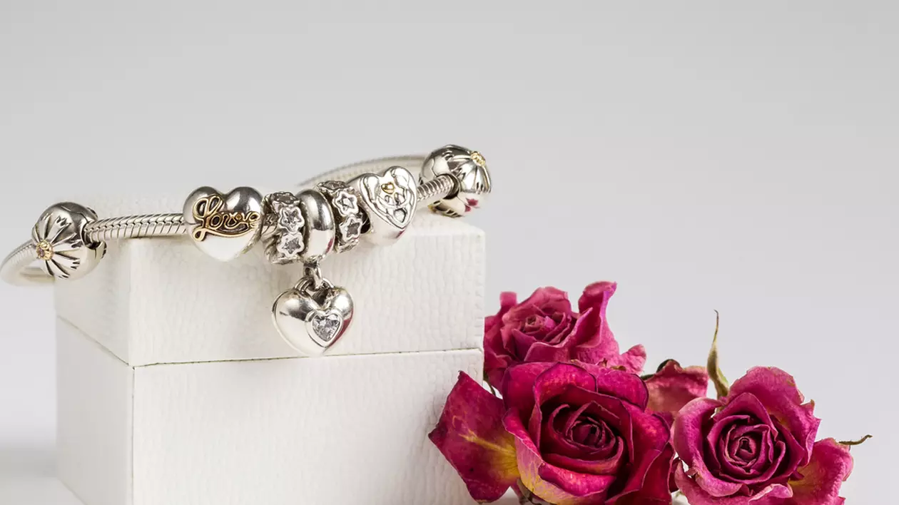 Brățari, talismane și accesorii Pandora la ofertă - Imagine cu o brăţară şi accesorii Pandora pe o cutie de culoare albă, alături de un buchet de trandafiri roşii