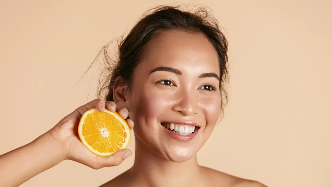 10 motive pentru care vitamina C ar trebui inclusă în rutina ta de îngrijire a pielii - Imagine cu o tânără care ţine lângă faţa ei o jumătate de portocală, sugerând beneficiile vitaminei C în îngrijirea pielii