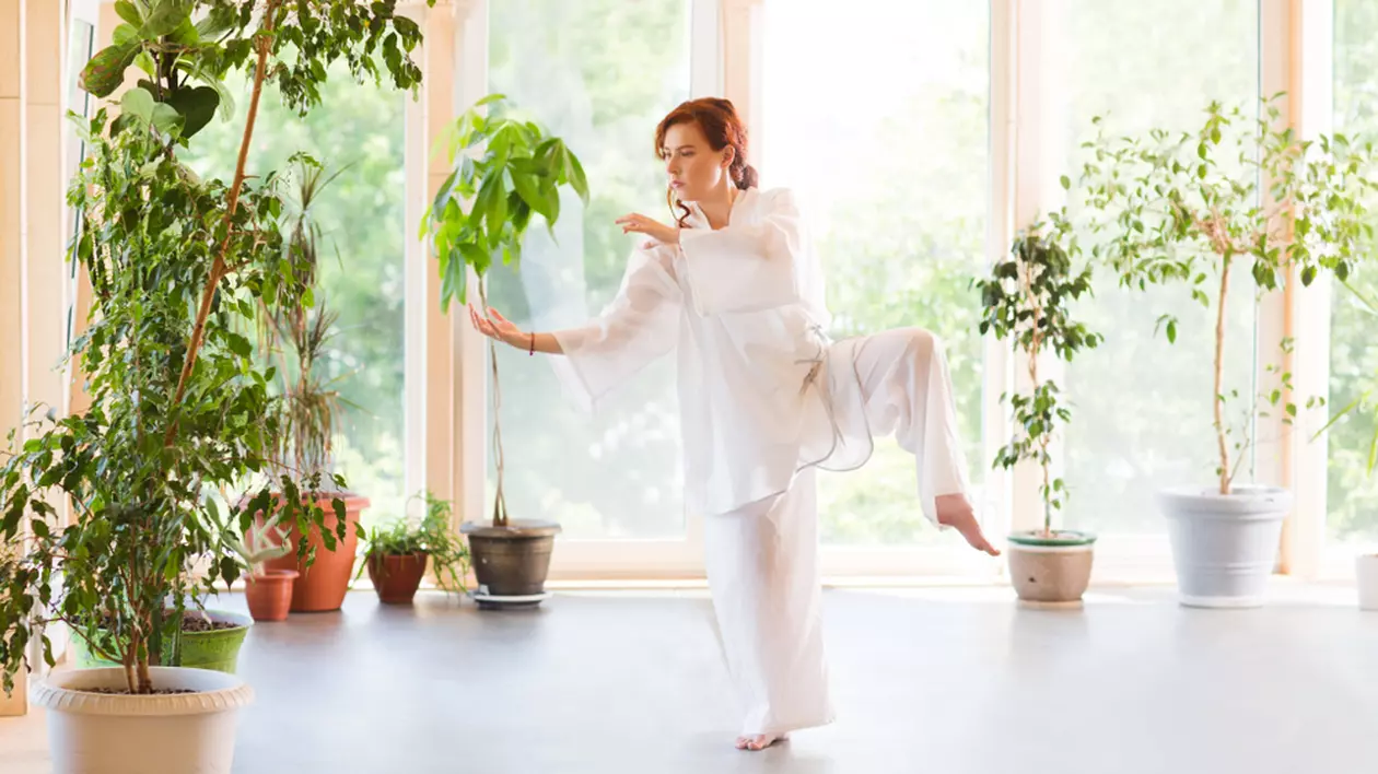 Ce este Tai Chi. Diferența dintre Tai Chi și Yoga - Imagine cu o tânără care practică Tai Chi la ea acasă.