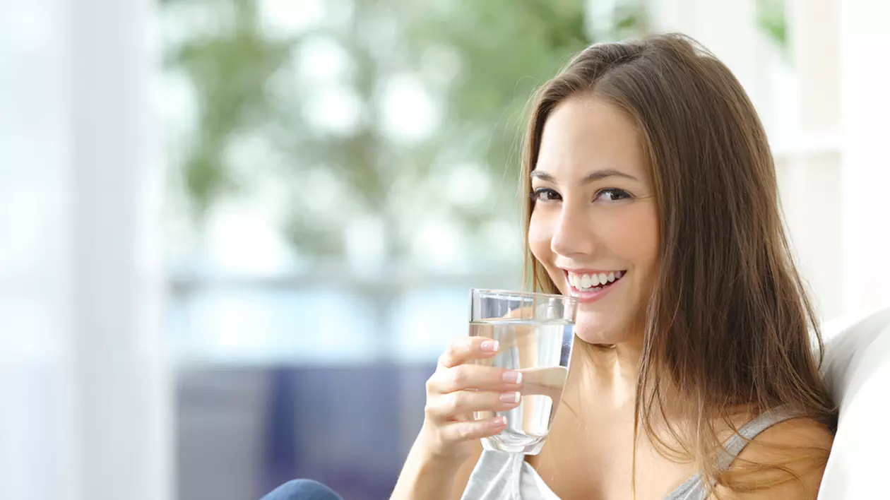 Diferența dintre apa de masă plată, apa de izvor și apa minerală naturală plată - Imagine cu o tânără zâmbitoare care bea un pahar de apă