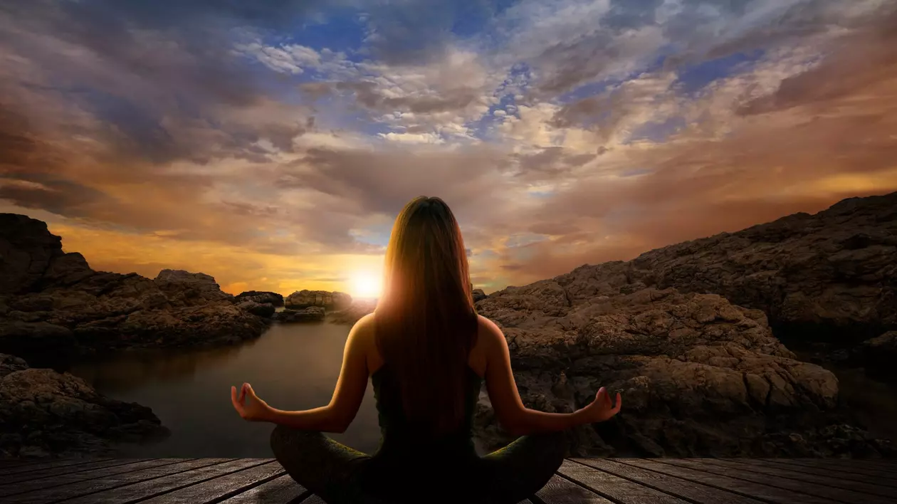 Diferența dintre meditație și mindfulness - Imagine cu o femeie care meditează în faţa unui peisaj cu un apus de soare