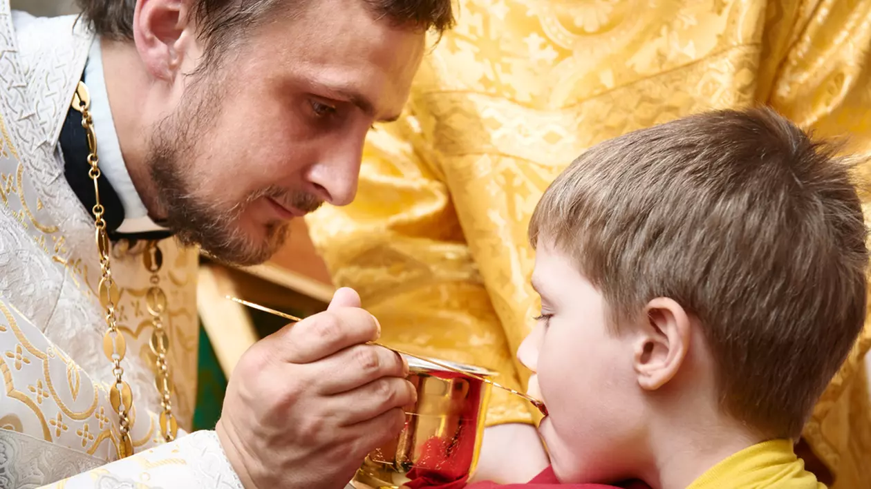 Sfânta Împărtășanie – reguli pentru credincioși - Imagine cu un preot care împărtăşeşte un copil