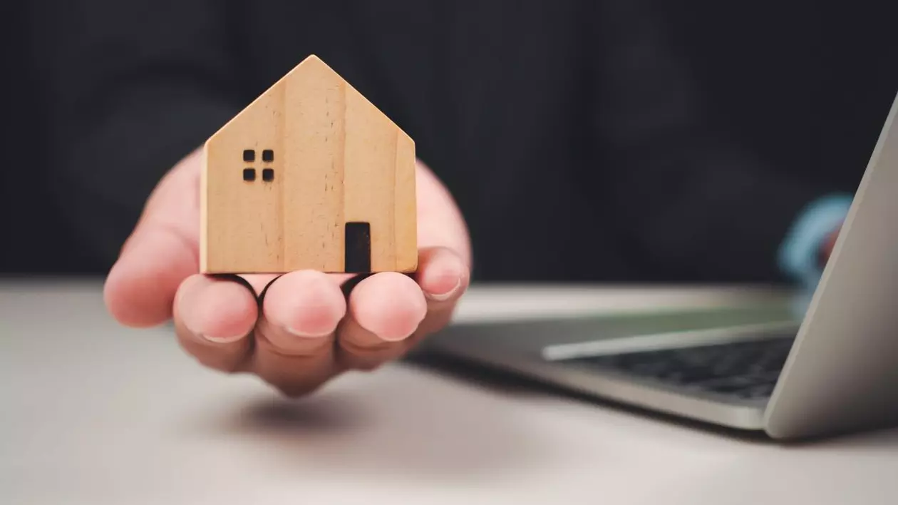 Ilustrație foto cu un agent imobiliar care prezintă un model de casă de jucărie lângă un laptop