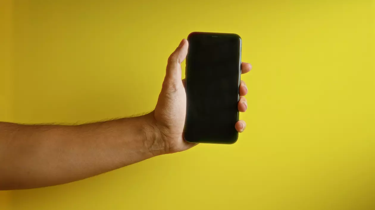 Telefoane sub 1.000 de lei la eMAG de Black Friday 2024 - Imagine cu un smartphone ţinut de o mână de bărbat pe un fond galben