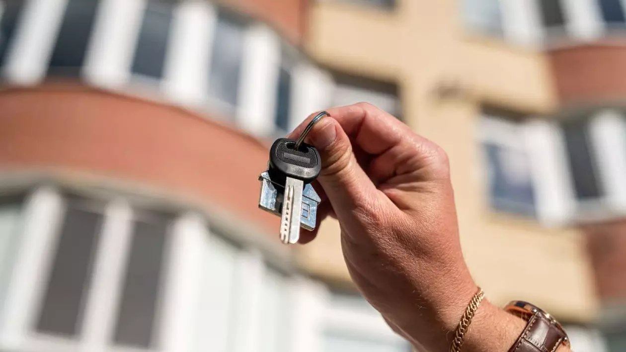 Un set de chei este ținut în mână fața unui bloc de apartamente