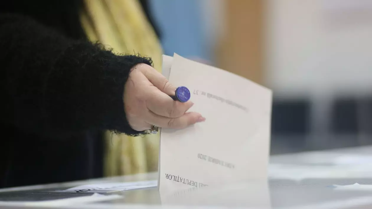 Prim plan cu o femeie care introduce în urnele de vot un buletin de vot, având în mână ștampila de vot