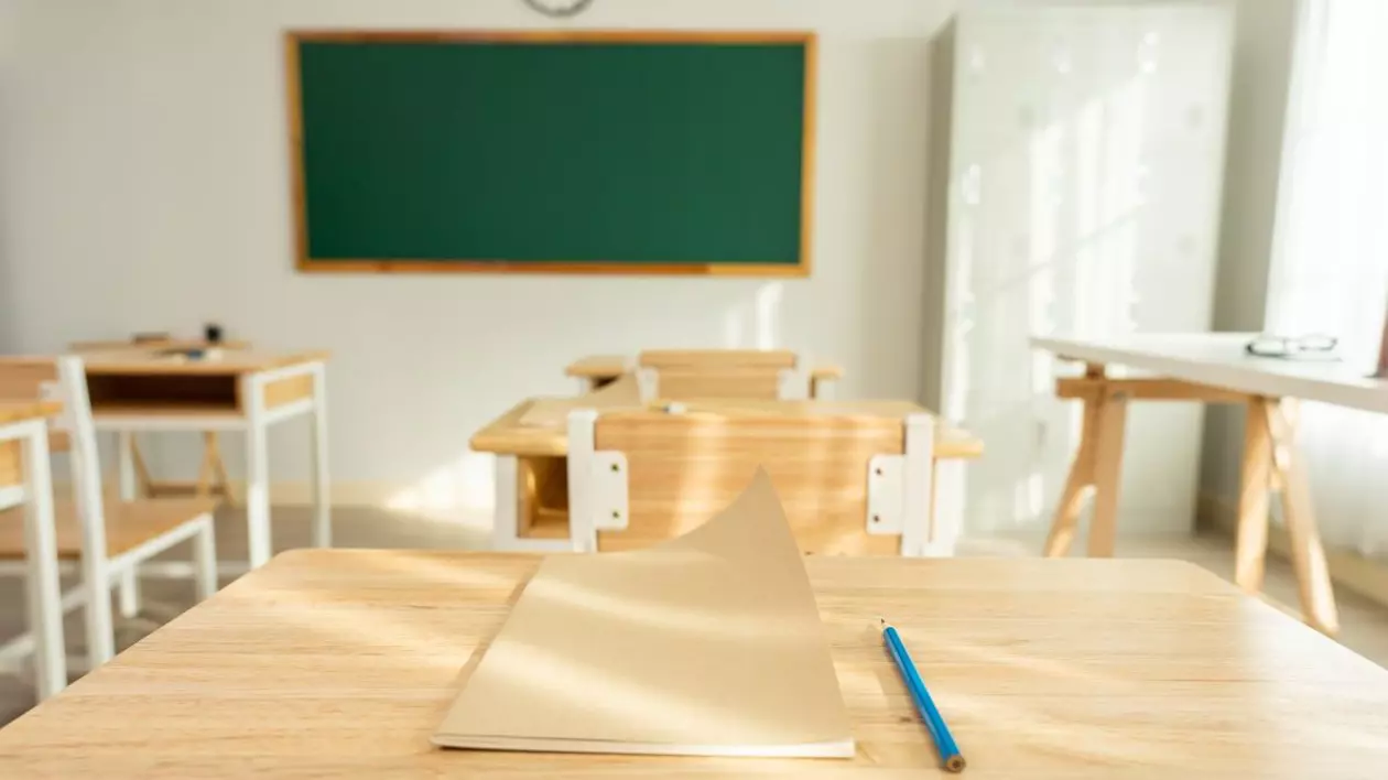 O sală de clasă cu tablă și bănci goale, în prim-plan un caiet și un creion albastru pe masă. Foto: Shutterstock